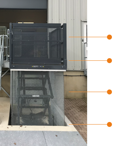Industrial dock lift with a mesh enclosure and labelled components, positioned outside a commercial building.