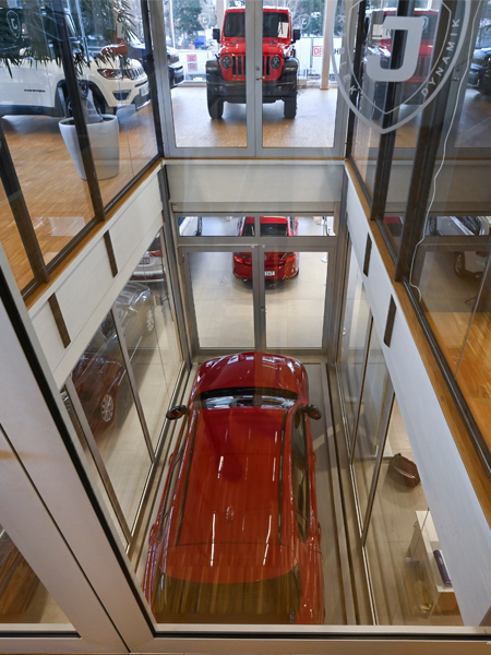 A red car being lifted by a goods lift inside a car warehouse