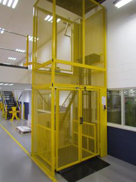 Yellow goods lift with a mesh enclosure in an industrial facility, providing secure transportation between levels.